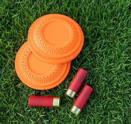 Clay disc flying targets and shotgun shells on green grass background